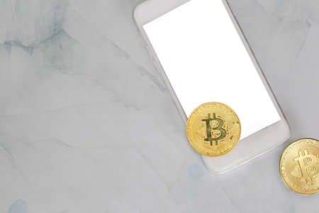 golden bitcoin lies on a smartphone on marble background top view with copy space, cryptocurrency or...