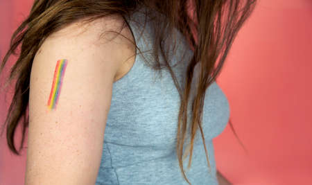 Portrait of a young woman with rainbow Flag on cheek and body, the LGBT community on a colorful pink...