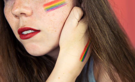 Portrait of a young woman with rainbow Flag on cheek and body, the LGBT community on a colorful pink backgroundの写真素材