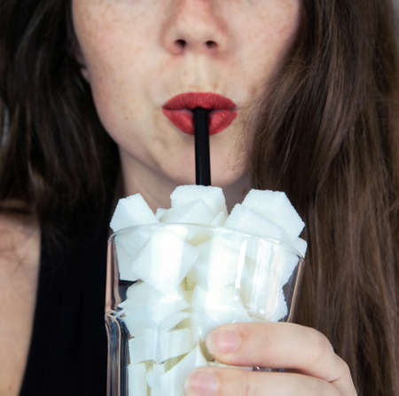 Portrait of young woman drinking with a black colored straw from a glass filled with sugar cubes Junk food, unhealthy diet, too much sugar on drinks, nutrition conceptの写真素材