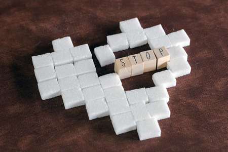 Sugar cubes in heart shape on brown background texture with Stop sign for diabetes. To stop...