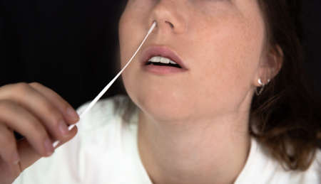 Young woman taking a Covid-19 SARS-CoV-2 test during Corona pandemic on dark black background, quick...