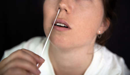 Young woman taking a Covid-19 SARS-CoV-2 test during Corona pandemic on dark black background, quick...