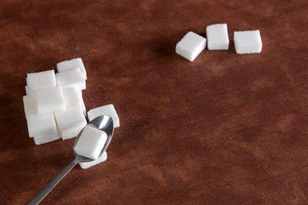 Sugar cubes with spoon top view on brown natural colored background texture with copy space, Sugar,sweet,health,food conceptの写真素材