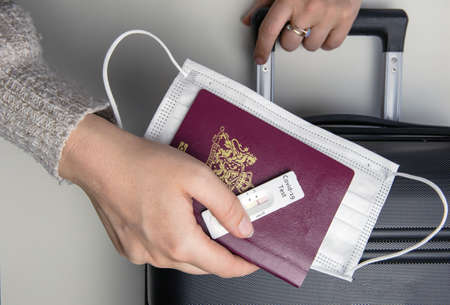 COVID-19, travel and lockdown concept, Young womans hand with passport, medical mask and negative...