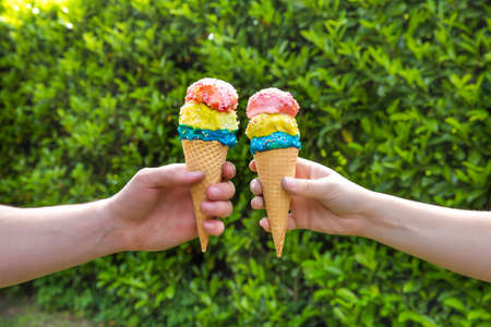 Couple with colorful different flavors of Ice Cream Cone with sprinkles with green leaf background,...