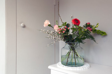 Beautiful spring flowers in glass a vase, near gray wall in stylish home, modern interior decoration...