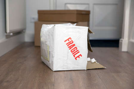 Beat up damaged delivery box with fragile sticker, broken deliverd cardboard packaging at homeの写真素材