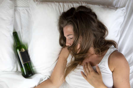 Sleeping drunk girl with empty wine bottle. Lying on the bed fainted, alcohol abuse,addiction...