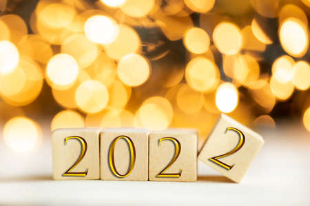 The year 2022 written on wooden cubes in gold luxury letters with shiny bokeh background, New Year...