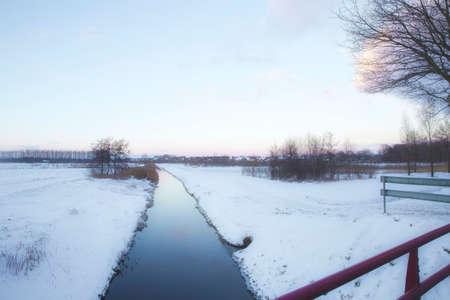 Beautiful winter landscape at sunset with fog and snow covering farmland and river in the Netherlands beautiful colors in natureの写真素材