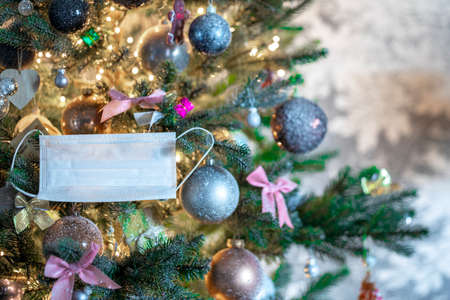 Merry Christmas in the new Covid-19 reality. Front view of a Christmas tree with protective white medical face mask in decorated tree 2021 coronavirus, Covid-19 with copy spaceの写真素材
