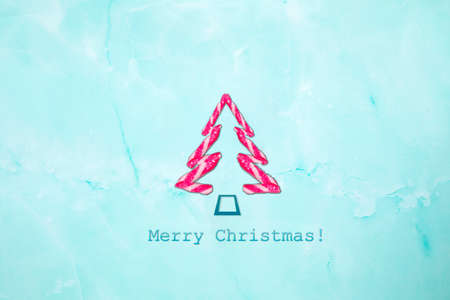 Merry Christmas text and shape Christmas tree of candy canes on light blue background. New Year...
