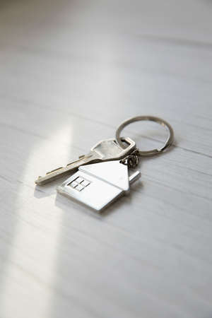 Silver key with silver house figure on white wooden background, buying new house real estate concept...