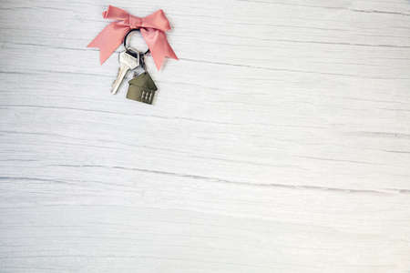 New keys of a house silver with keychain of little house top view with copy space and white wooden background, space for textの写真素材