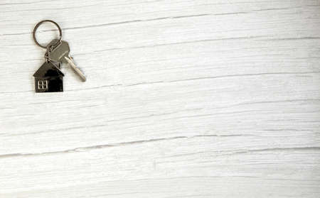 Silver key with silver house figure on white wooden background, buying new house real estate concept...