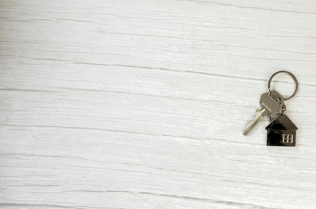 Silver key with silver house figure on white wooden background, buying new house real estate concept copy spaceの写真素材