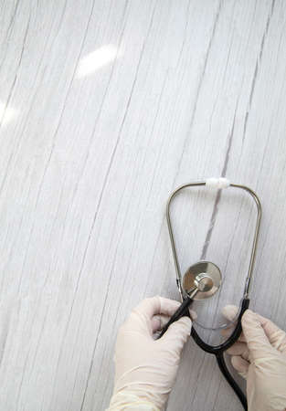 White protective medical gloves holds a stethoscope on a white wooden background. Concept visit to the doctor, virus, treatment, diagnosis. Banner. Flat lay, top view copy spaceの写真素材