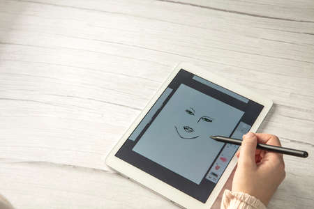 Young creative designer holding stylus pen drawing on screen of digital tablet on wooden desk with copy space, modern digital art top view space for textの写真素材