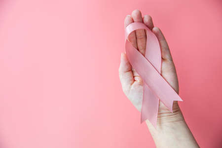 Female hands holding pink ribbon over pink background, breast cancer awareness, October pink concept top view with copy space, health, woman cancer conceptの写真素材