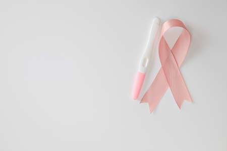 Pink satin breast cancer awareness ribbon with blank pregnancy test isolated on white background top...