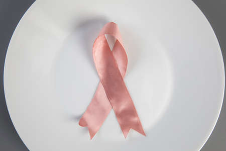 Pink ribbon on white plate with knife and fork. Breast cancer awareness concept top view, medical health and food conceptの写真素材