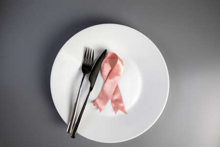 Pink ribbon on white plate with knife and fork. Breast cancer awareness concept top view, medical health and food conceptの写真素材