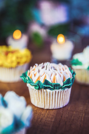 Various cupcakes decorated with colorful flower icing on wooden table, floral bouquet, wedding cake,...