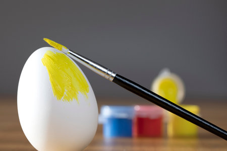 rough brush is painting a fragile easter egg with Yellow color, prepering for Holiday Happy Easter concept closeup colorful hobbyの写真素材