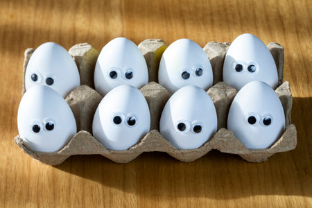 Funny faces on white eggs in carton box with organic chicken eggs on kitchen table closeup big animation eyes. humour, food and easter holiday concept. close-upの写真素材