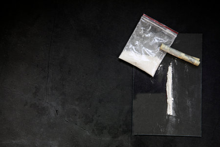 Cocaine powder lines, rolled banknote and drugs in plastic bag pocket on black glass surface background, top view. Drug addiction concept darkの写真素材