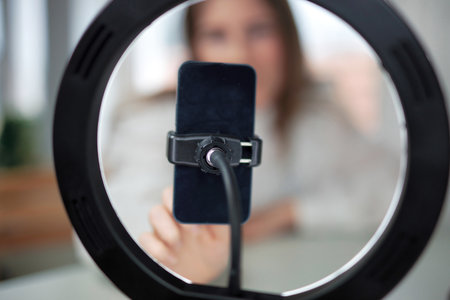 Lifestyle beauty blogger streaming online from home studio. Diverse millennial woman working as make up artist and recording video for social media on smartphone with led ring lamp, blogging content creator influencer social mediaの写真素材