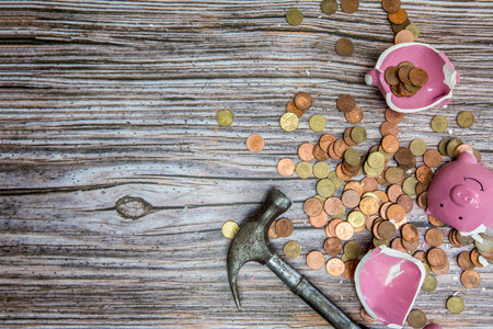Broken piggy bank smashed into pieces with hammer, with cash and coins on wooden background top view with copy space, money savings concept space for textの写真素材
