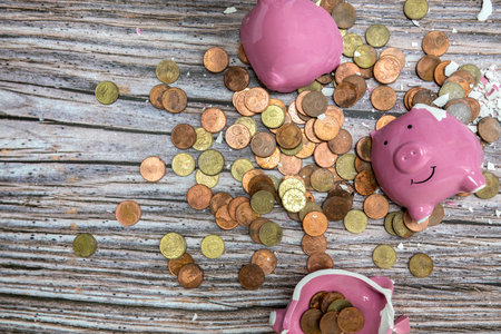 Broken piggy bank smashed into pieces with hammer, with cash and coins on wooden background top view with copy space, money savings concept space for textの写真素材