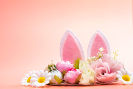 Spring holidays creative background with bunny ears decorated with bloom flowers on pastel pink...