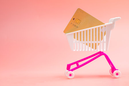 Shopping trolley cart with credit card on pink background. concept for online shopping. delivery, supermarket, paying with credit card, space for textの写真素材
