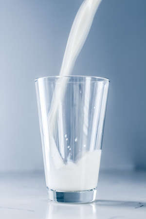 Dairy, healthy nutrition and breakfast concept - World Milk Day, pouring into glass on marble tableの写真素材