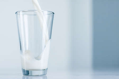 Dairy, healthy nutrition and breakfast concept - World Milk Day, pouring into glass on marble tableの写真素材