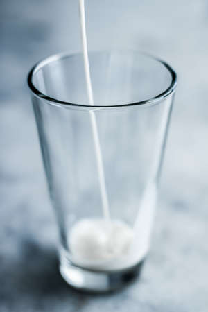 Dairy, healthy nutrition and breakfast concept - World Milk Day, pouring into glass on marble tableの写真素材