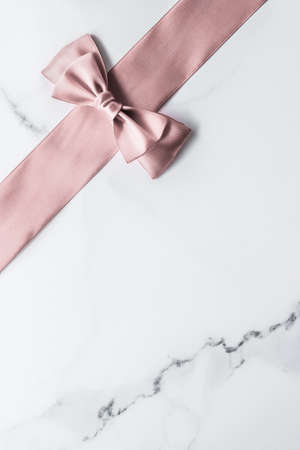 Birthday, wedding and girly branding concept - Beige silk ribbon and bow on marble background,...