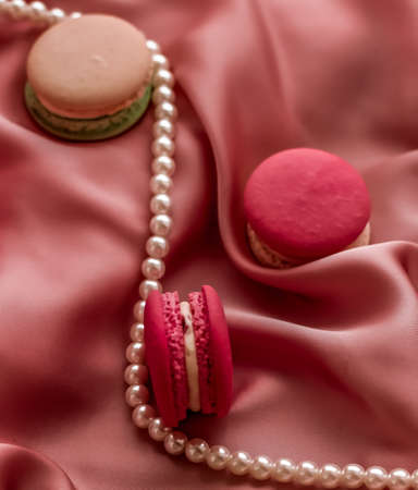 Girly, bakery and branding concept - Sweet macaroons and pearls jewellery on silk background, parisian chic jewelry, French dessert food and cake macaron for luxury confectionery brand, holiday giftの写真素材