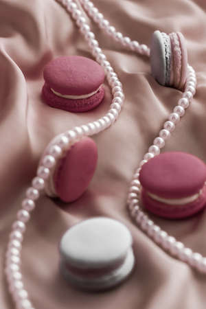 Girly, bakery and branding concept - Sweet macaroons and pearls jewellery on silk background, parisian chic jewelry, French dessert food and cake macaron for luxury confectionery brand, holiday giftの写真素材