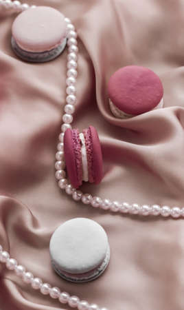 Girly, bakery and branding concept - Sweet macaroons and pearls jewellery on silk background, parisian chic jewelry, French dessert food and cake macaron for luxury confectionery brand, holiday giftの写真素材