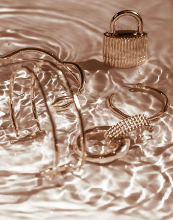 Jewellery branding, fashion gift and luxe shopping concept - Golden bracelets, earrings, rings, jewelery on gold water background, luxury glamour and holiday beauty design for jewelry brand adsの写真素材