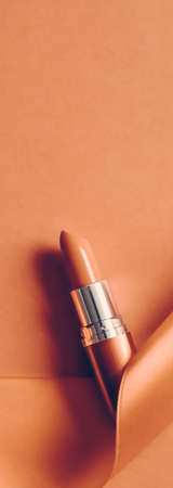 Cosmetic branding, glamour lip gloss and shopping sale concept - Luxury lipstick and silk ribbon on orange holiday background, make-up and cosmetics flatlay for beauty brand product designの写真素材