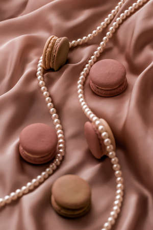 Girly, bakery and branding concept - Sweet macaroons and pearls jewellery on silk background, parisian chic jewelry, French dessert food and cake macaron for luxury confectionery brand, holiday giftの写真素材