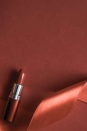 Cosmetic branding, glamour lip gloss and shopping sale concept - Luxury lipstick and silk ribbon on bronze holiday background, make-up and cosmetics flatlay for beauty brand product designの写真素材