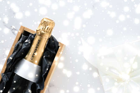 New Years Eve, happy holidays and luxury present concept - Christmas holiday champagne bottle and a gift box and shiny snow on marble backgroundの写真素材
