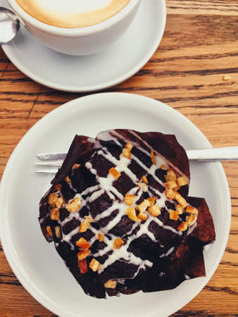 Cup of coffee and chocolate muffin on wooden table in city cafe