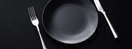 Empty plates and silverware on black background, premium tableware for holiday dinner, minimalistic...